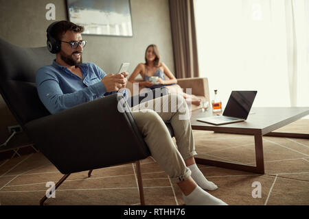 Smiling man utilise un téléphone avec écouteurs pour écouter de la musique et vous détendre à la maison Banque D'Images