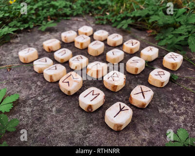 Une pile de runes en bois de forêt. Runes en bois reposent sur un fond de roche dans l'herbe verte. Les runes sont taillées dans des blocs de bois. Sur chaque rune symbole pour Banque D'Images