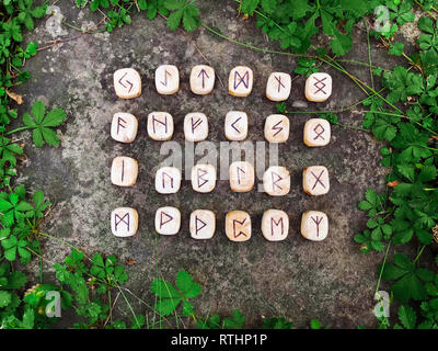 Une pile de runes en bois de forêt. Runes en bois reposent sur un fond de roche dans l'herbe verte. Les runes sont taillées dans des blocs de bois. Sur chaque rune symbole pour Banque D'Images