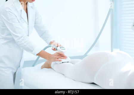 Cosmetologist femelle méconnaissable faisant Rf Procédure de levage sur femme s longues et fines jambes dans un salon de beauté. Traitement de l'embonpoint et flasque de la peau. Banque D'Images