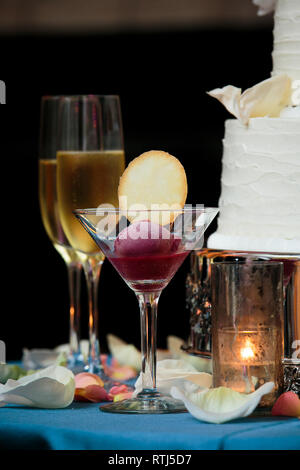 Un verre avec un sorbet et un cookie avec des verres de champagne et un gâteau de mariage dans l'arrière-plan a servi lors d'un mariage de fantaisie Banque D'Images