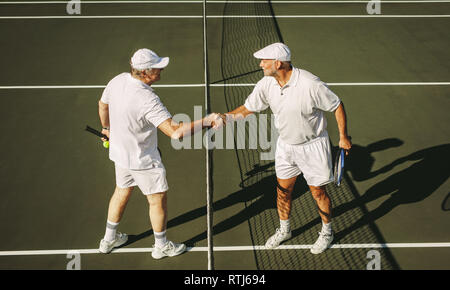 Vue latérale des deux joueurs de tennis senior se serrer la main sur un court de tennis. Les hommes sur un court de tennis, debout près de la poignée de mains nettes. Banque D'Images