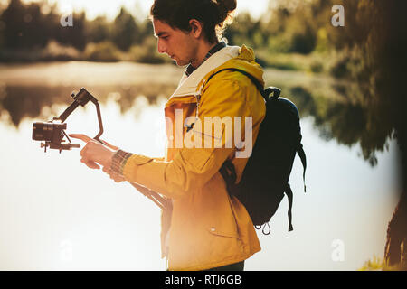 Vue latérale d'un voyageur de prendre des photos sur une tourelle stabilisateur pour caméras. Portrait d'un homme tenant un stabilisateur pour caméras pour filmer un appareil de cardan Banque D'Images