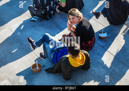 Parler des gens assis au soleil sur les marches à côté du Regents Canal devant le charbon tombe Yard, Kings Cross, Londres, Angleterre Banque D'Images