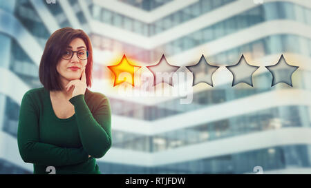 Skeptic Jeune femme tenant la main sous le menton à déçu le choix d'un classement par étoiles. Mauvais service à la clientèle faible et concept. Sentiment négatif, di Banque D'Images