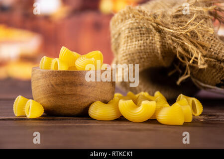 Beaucoup de entier jaune pâtes crues pipe rigate variété avec bol en bois dans la cuisine en bois rustique Banque D'Images