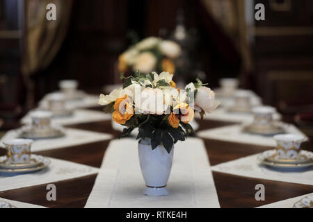 Une table élégante, pour une réunion formelle avec une magnifique pièce maîtresse florale dans un vase blanc qui se compose principalement de fleurs de couleur claire et florissantes, y compris des variétés telles que des pivoines, des roses, complétées par des coquelicots. Bélarus Banque D'Images