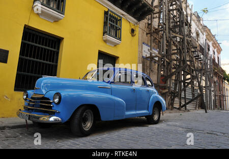 Une voiture classique se trouve garé dans une rue de la Vieille Havane, Cuba, près de l'échafaudage en bois érigé pour la restauration à un bâtiment délabré. Banque D'Images