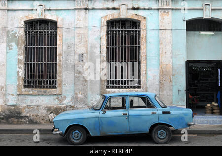 Une vieille voiture bleue se trouve garé dans une rue de la Vieille Havane, Cuba, en face d'un bâtiment non restaurés avec grand, barreaux aux fenêtres. Banque D'Images