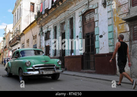 Un homme marche dans une rue typique bordée de bâtiments historiques dans la Vieille Havane, Cuba comme une voiture classique durs passé. Banque D'Images