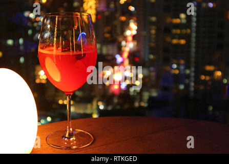 Verre de rouge vibrant cocktail sur la table du bar sur le toit avec vue sur la nuit urbaine en arrière-plan flou Banque D'Images