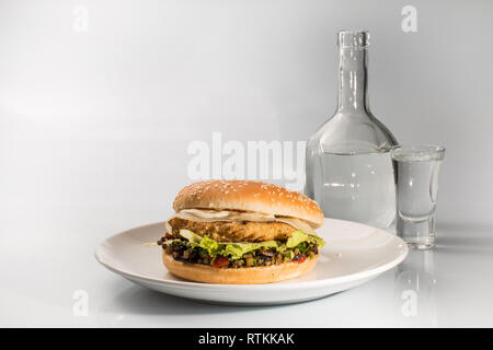 Cheeseburger sur une plaque avec patty de boeuf et de concombres, en tranches, avec un verre sur un fond isolé Banque D'Images