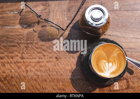 Vue de dessus de tasse de lait chaud avec du café latte art, smartphone, les lunettes et le sucre brun sur un bureau en bois dans la lumière du matin Banque D'Images