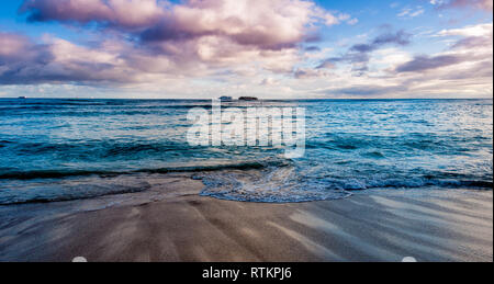 Briser les vagues sur la célèbre plage de Waikiki à Oahu au coucher du soleil. Banque D'Images