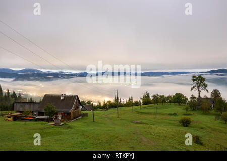 Panorama de montagne d'été. Petite maison en bois et chalet grange sur la montagne verte vallée le brouillard, nuages ciel lumineux et crête de montagne copie espace backg Banque D'Images