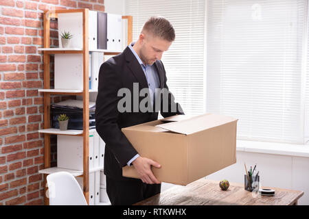 Malheureux jeune homme transportant ses affaires dans la boîte en carton sur le lieu de travail Banque D'Images