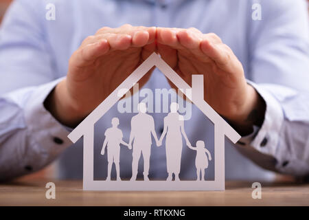 Close-up of a Businessman Protéger Family Paper Cut Out avec les mains de bureau en bois Banque D'Images