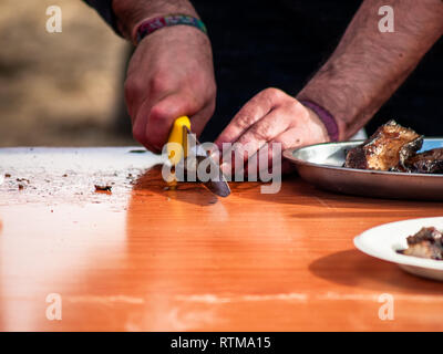 Personne méconnaissable couper la viande avec un couteau et placez-le sur une assiette en carton dans la rue à une fête populaire dans un village de l'Espagne Banque D'Images