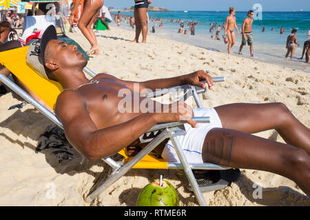 RIO DE JANEIRO - le 25 janvier 2015 : un jeune homme musclé brésilien se trouve dans une chaise de plage à bronzer sur un bel après-midi sur la plage d'Ipanema. Banque D'Images