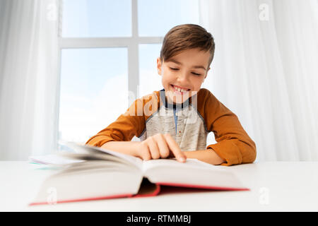 Student boy reading book at home table Banque D'Images