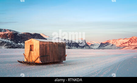 Cabane de pêche abandonnés assis sur la mer gelée lorsque le soleil se couche. Banque D'Images