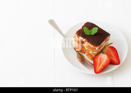 Tiramisu italien sucré fait maison, dessert sans cuisson gâteau au fromage, de couper le gâteau sur une petite plaque ornée de menthe fraîche et un peu de fraises, sur wh Banque D'Images