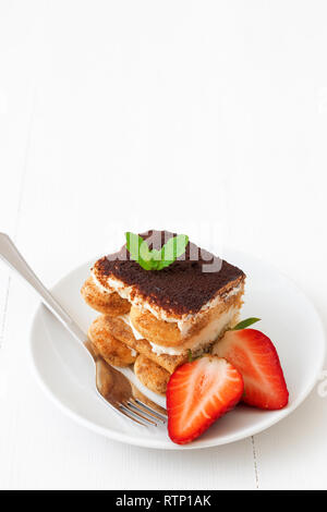 Tiramisu italien sucré fait maison, dessert sans cuisson gâteau au fromage, de couper le gâteau sur une petite plaque ornée de menthe fraîche et un peu de fraises, sur wh Banque D'Images