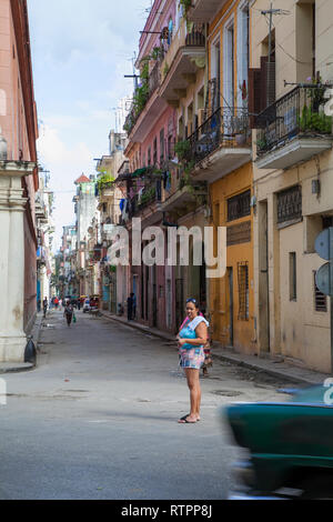 La Havane, Cuba - 06 janvier 2013 : une vue sur les rues de la ville avec des cubains. Une femme se tient debout au milieu de la rue, un taxi dans la fo Banque D'Images