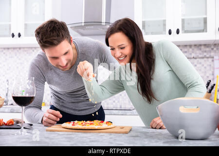 Saupoudrer le fromage sur le couple Smiling In Pizza Banque D'Images
