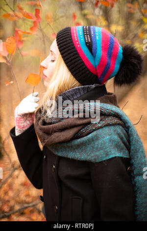 Fille blonde respire le parfum de l'automne les feuilles d'un arbre dans la forêt Banque D'Images