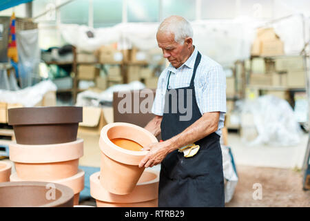 Homme plus âgé en tablier noir le choix de pots pour fleurs et arbres en marché de jardinage Banque D'Images