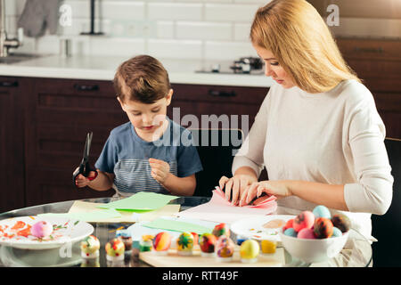 Joyeux petit garçon de 4 ans l'apprentissage de l'utilisation de ciseaux avec une maman, découpe du lapin de Pâques colorés sous forme papier. Famille heureuse s'asseoir Banque D'Images