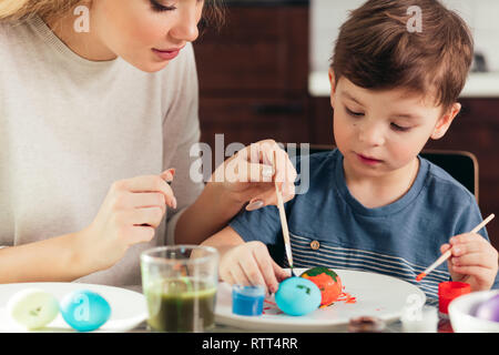 Belle blonde jeune mère et son fils de quatre ans mignon s'amuser tandis que la peinture des œufs de Pâques, à la cuisine, en souriant, un créatif Banque D'Images