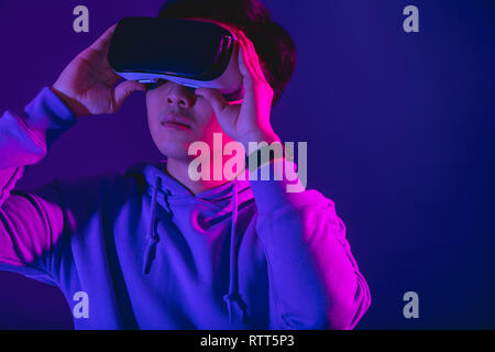 Jeune asiatique s'énerver pendant 3 regarder d film à l'aide de casque de réalité virtuelle, posant sur fond violet foncé isolés. Banque D'Images