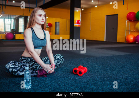 Shot of young woman stretching à la salle de sport. Femme exercisesto musculaire faisant étirer son corps sur le sol. Femme groupes à fitness gym Banque D'Images