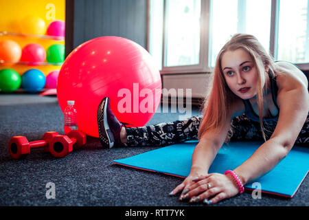 Shot of young woman stretching à la salle de sport. Femme exercisesto musculaire faisant étirer son corps sur le sol. Femme groupes à fitness gym Banque D'Images
