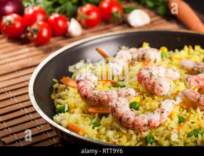 Riz blanc cuit aux crevettes, curry et de légumes dans une casserole sur un fond de bois de bambou marron. Banque D'Images