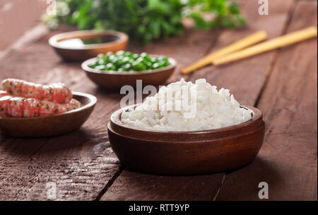 Riz blanc cuit dans bol en bois aux crevettes, pois et baguettes de bois sur un fond brun. Banque D'Images