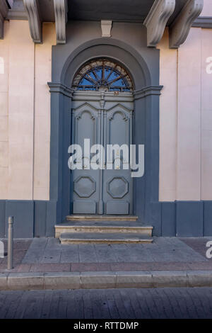 Grand arqua porte en bois. Style traditionnel chypriote dans les villes. Peint en gris avec un mur rose pâle. Banque D'Images