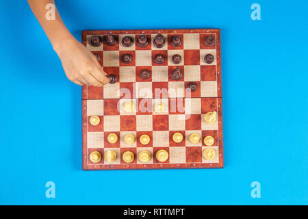 Kid mains sur un échiquier jouant aux échecs sur fond bleu, vue d'en haut Banque D'Images