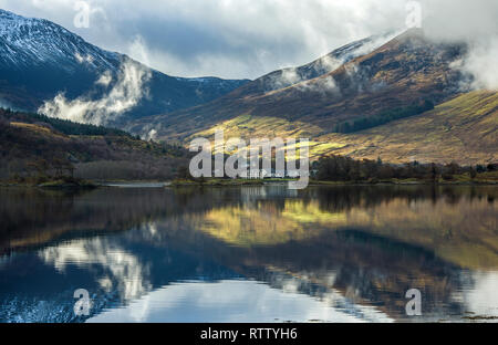 Réflexions claires les montagnes et les arbres sur le Loch Leven, Glencoe, sur un éclairage magnifique journée d'hiver en février. Banque D'Images