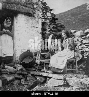 La vie réelle de l'économie domestique en Irlande 1904 une femme assise à une roue qui tourne à l'extérieur d'un chalet au toit de chaume dans l'Irlande rurale Banque D'Images