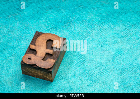 La livre sterling du symbole dans la typographie type de bloc d'impression turquoise contre du papier fait à la main avec une copy space Banque D'Images