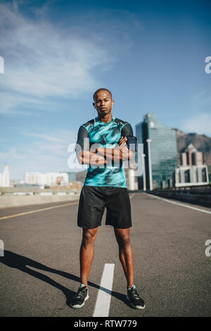 Portrait de l'homme urbain runner standing dans la rue au matin. Young sportsman debout dans la rue, les bras croisés. Banque D'Images