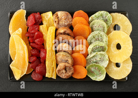 Fruits confits morceaux de mangue, papaye, kiwi, ananas, fraises, figues séchées, abricots, allongé sur une plaque en céramique noire sur une pierre noire surface. M Banque D'Images