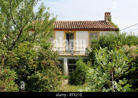 La maison de famille abandonnée avec portes en bois fissuré délabrées et fermé les stores complètement entouré de plantes et d'arbres à chenilles Banque D'Images