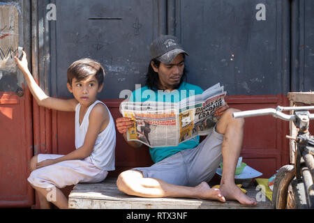 Un homme de son pays lit un document papier tout en s'asseyant dans un bidonville, Cebu City,Philippines Banque D'Images