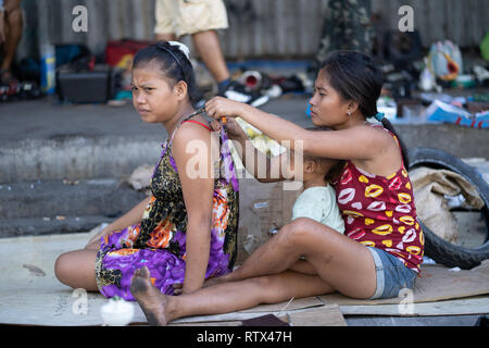 Deux femmes aux Philippines, l'un sans chaussures, et un enfant s'asseoir sur du carton dans une rue latérale, Cebu City, Philippines Banque D'Images