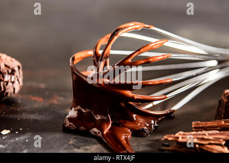 Revêtement épais chocolat fondu un vieux fouet de métal couché sur un comptoir de cuisine en bois avec des morceaux de chocolat et un bonbon Banque D'Images