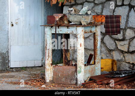 Étau rouillé monté sur table en métal entouré de vieux matériaux de construction et déchets le mur en pierre et la porte verrouillée background Banque D'Images